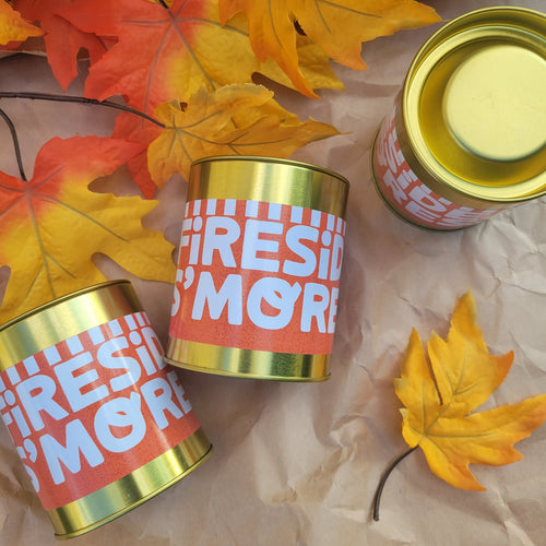 Three gold metal cans with red and white 'FIRESI 'MOR'E' labels arranged on brown paper with autumn maple leaves. One can is open, showing a pale yellow cream-colored product inside, while the others are closed.