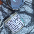 Two cosmetic jars styled on a white surface with black spiderweb fabric and a skull prop. One round jar has a dark lid with a small blue bird logo, and the other cylindrical jar has a white label reading 'TESTING FACE' in black letters.
