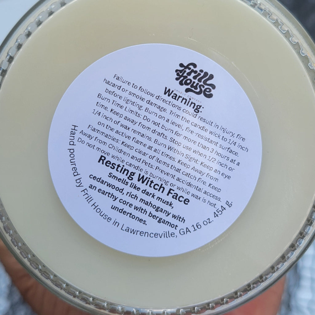 A hand holding a round tin of 'Healing Witch Face' face wax. The product is a creamy off-white color inside a silver metal tin with a white circular label.