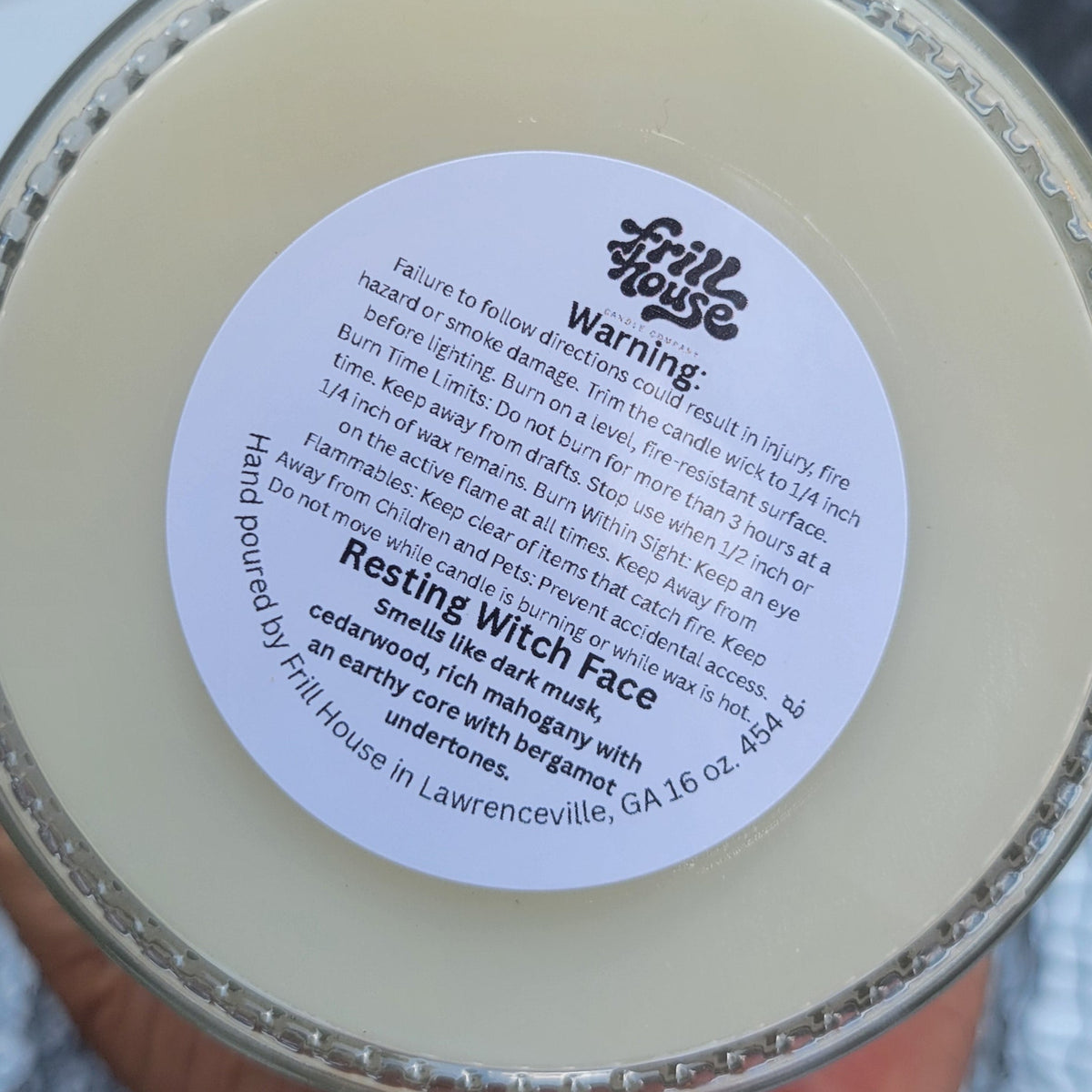 A hand holding a round tin of 'Healing Witch Face' face wax. The product is a creamy off-white color inside a silver metal tin with a white circular label.