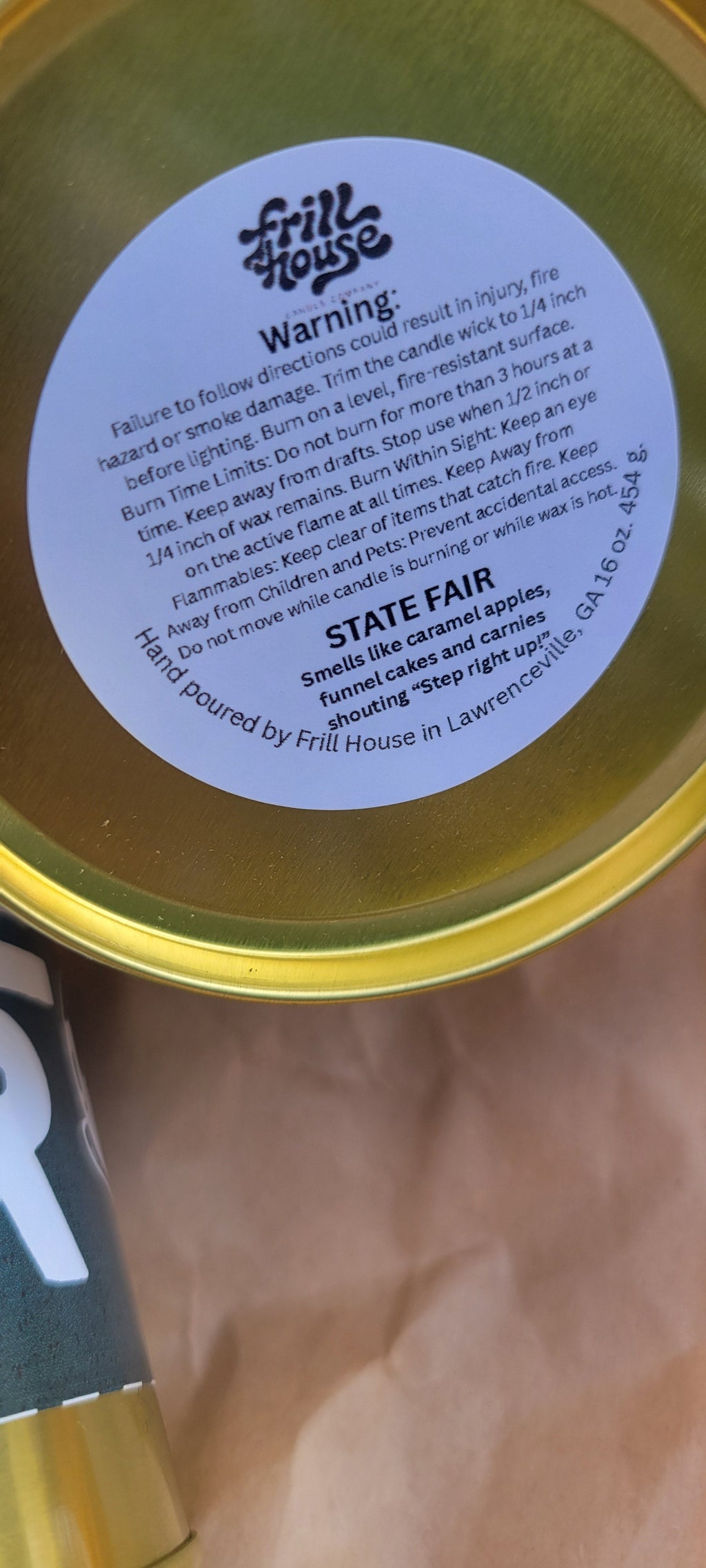 A close-up of a round gold tin with a white circular label reading 'WARNING' and 'STATE AIR', resting on a brown paper surface.