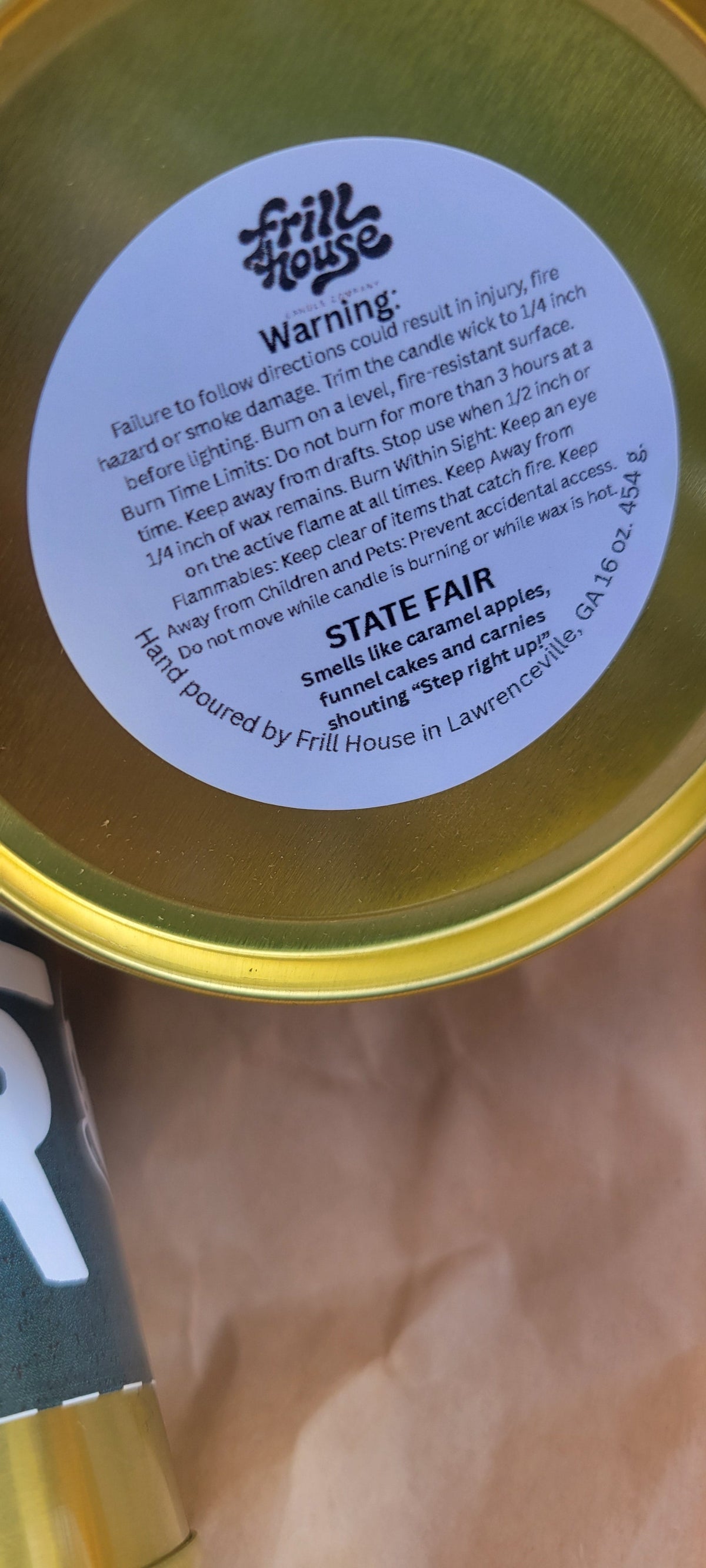 A close-up of a round gold tin with a white circular label reading 'WARNING' and 'STATE AIR', resting on a brown paper surface.